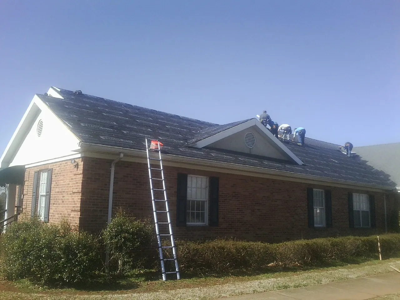 Crew tearing shingles off a brick ranch roof with a ladder set — Emergency Roof Repair work by our crew in West Bend