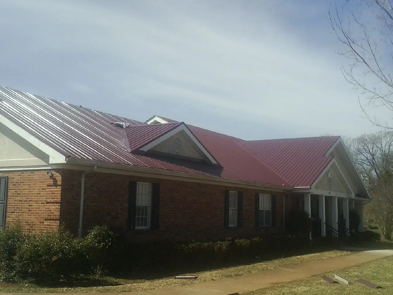 Red metal roof with gabled entries on a long brick building, from a Hail Damage Roof Repair job in West Bend