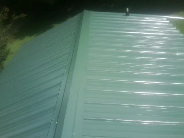 New green metal panels meeting at the ridge of a roof — Flat Roof Repair work by our crew in West Bend
