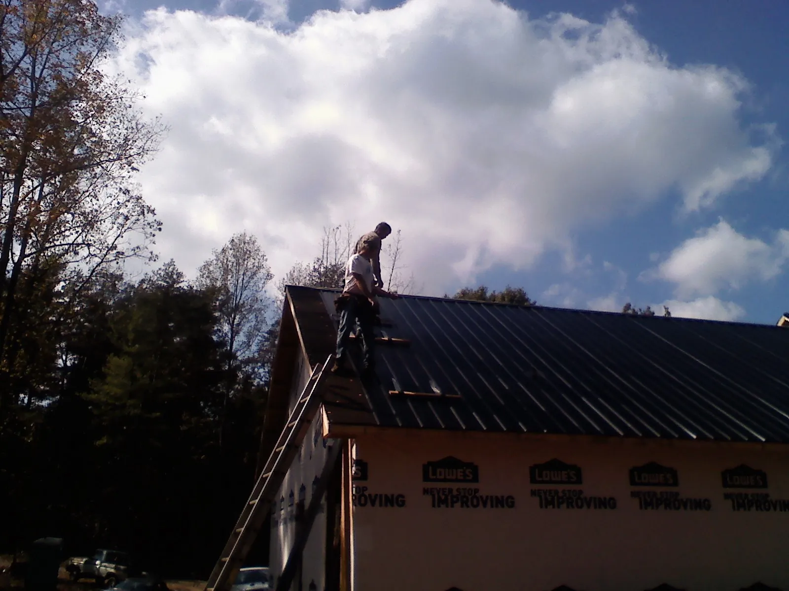 Roofer fastening dark metal panels high against a cloudy sky, from a Roof Inspection job in West Bend