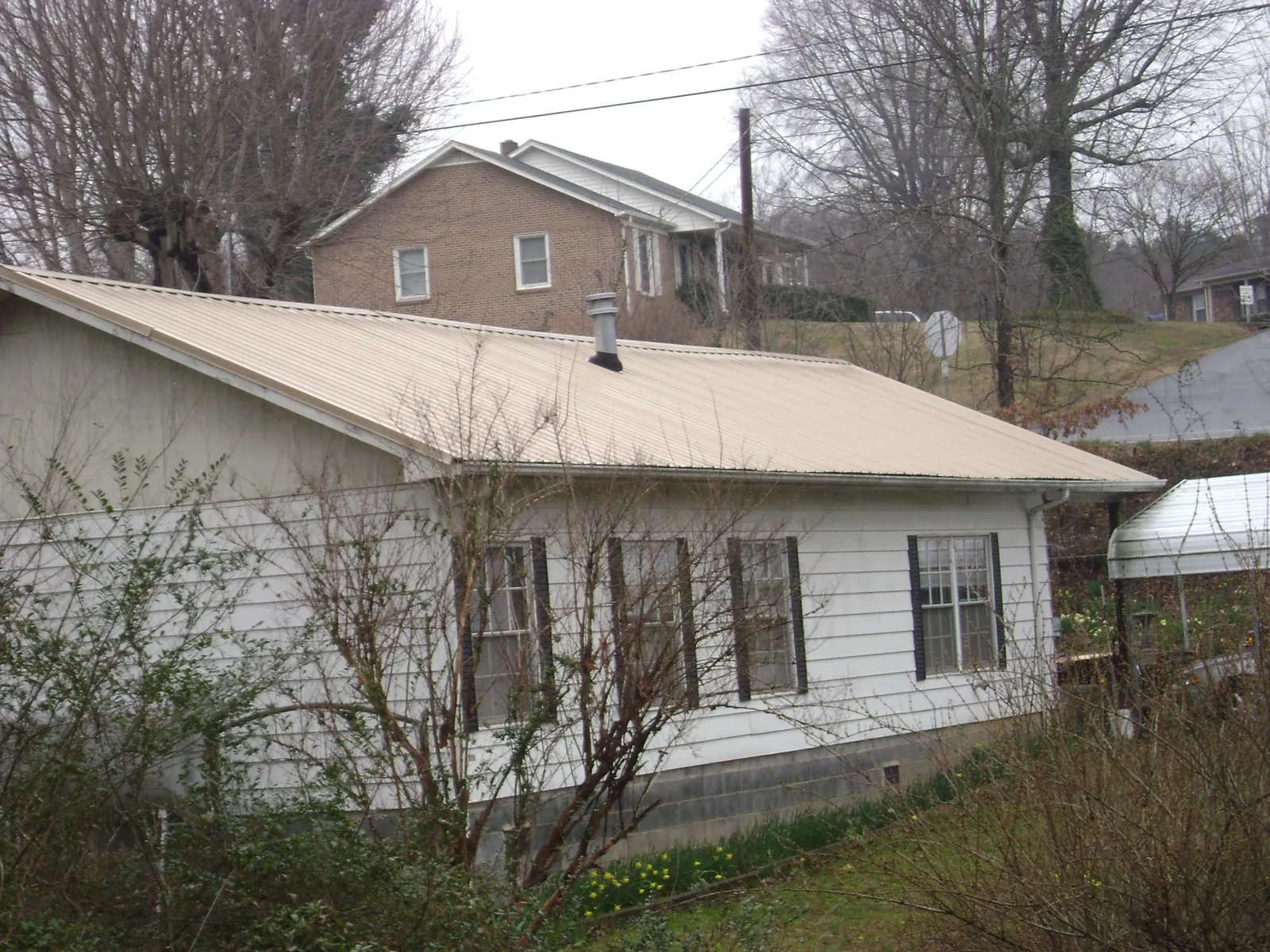 Tan metal roof on a white sided house set into a hillside — Commercial Roofing by Roofing Brothers in West Bend